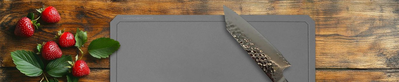 Dunkles HARDBOARD Schneidebrett mit Messer und Erdbeeren auf rustikalem Holztisch – natürliche Küchenästhetik.